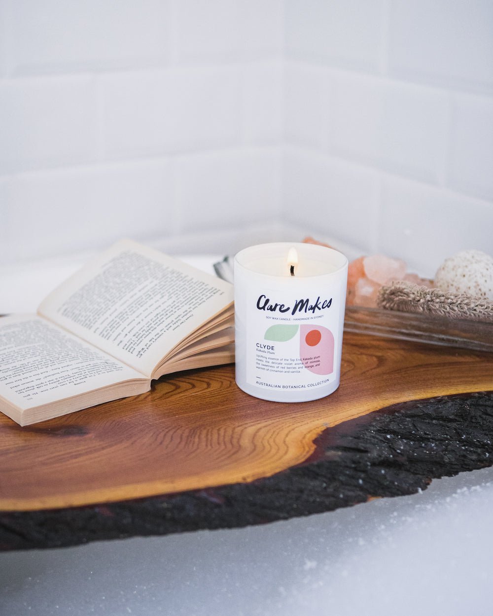 Clare Makes candle in Kakadu Plum scent styled on timber tray in a spa setting, with tiled wall