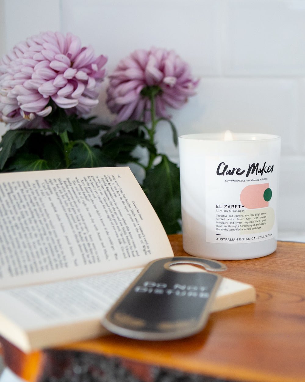 Elizabeth candle by Clare Makes, surrounded by pink flowers and a book