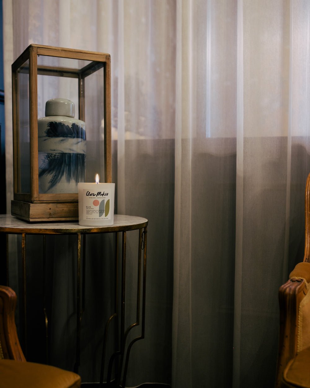 Ellis: Ghost Gum Breeze candle by Clare Makes on a black stool in front of sheer white curtains.