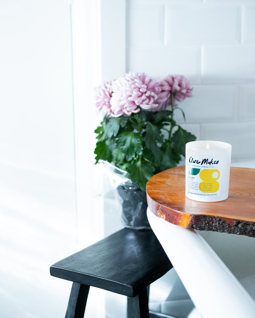 Henry candle by Clare Makes next to vase of flowers, styled in a bright and modern room