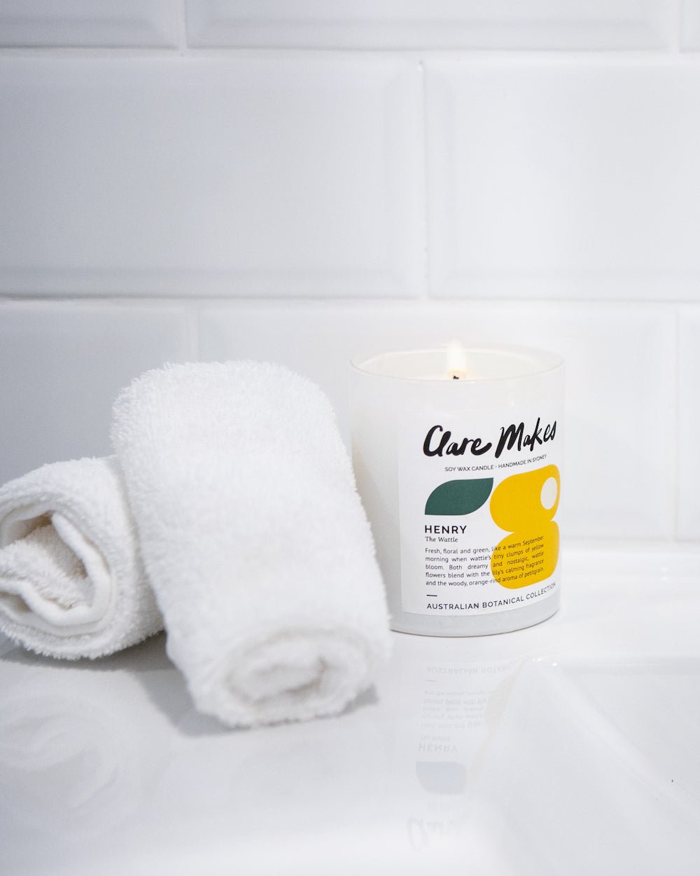 Henry candle by Clare Makes with The Wattle scent, styled with towels and gift box on a bathroom counter