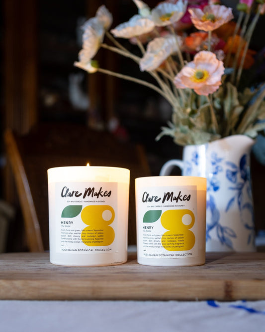 Pair of Clare Makes Henry candles with yellow wattle flowers on timber shelf for warm, nostalgic styling